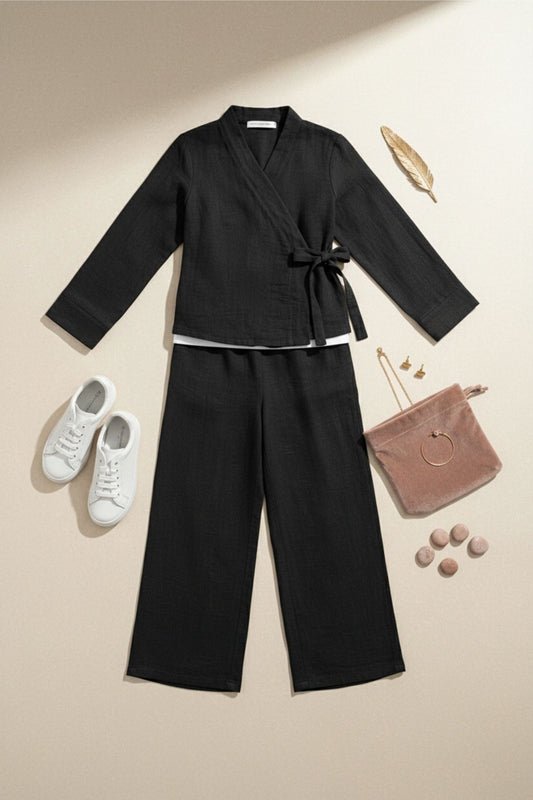 Black outfit with wide-leg pants, white sneakers, and a pink handbag on a beige background