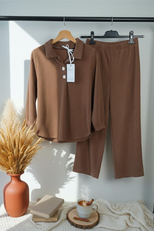 Brown suit on hangers with a vase, books, and cup on a table.