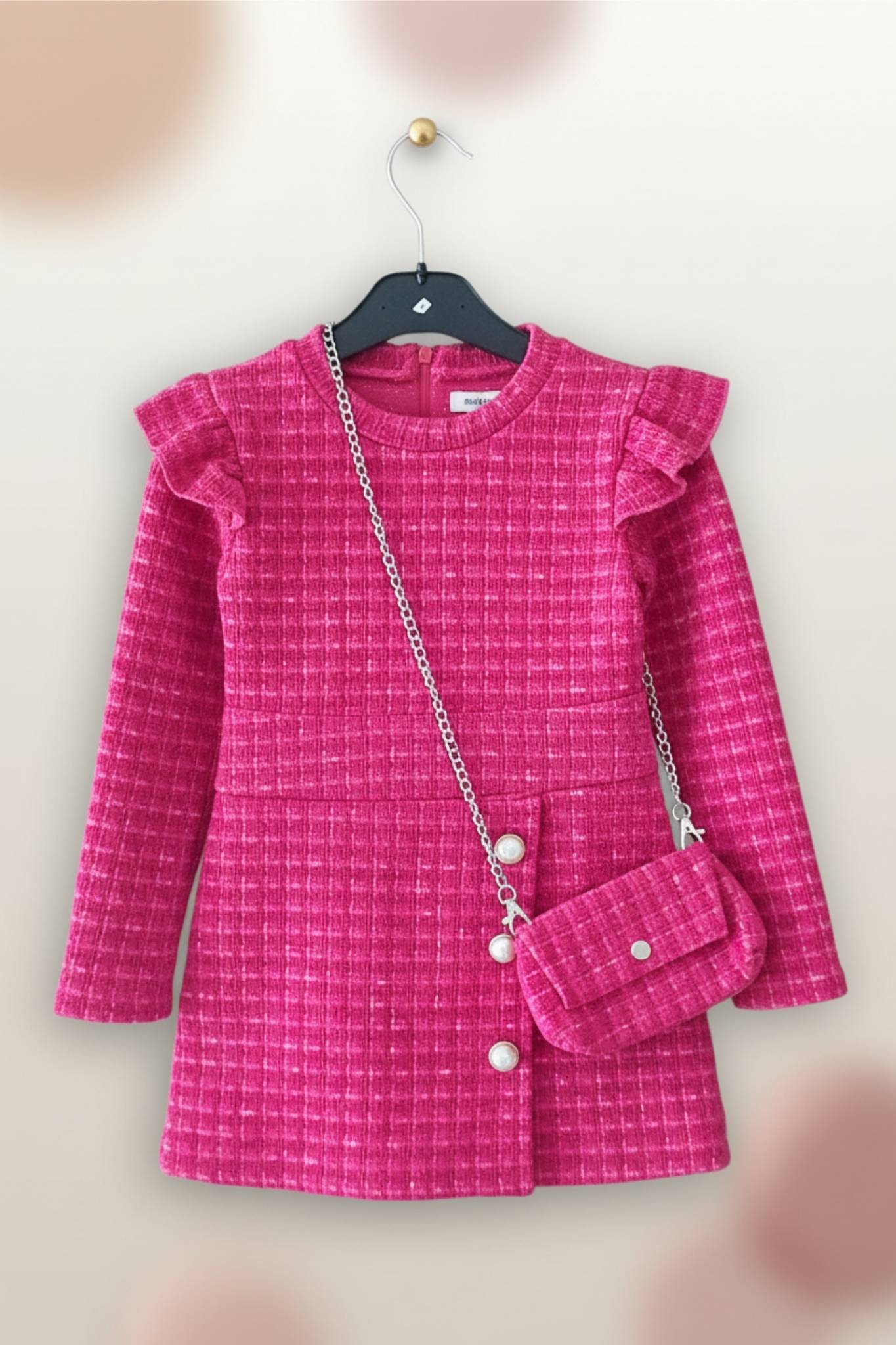 Pink dress with ruffled shoulders and matching handbag on a hanger against a beige background