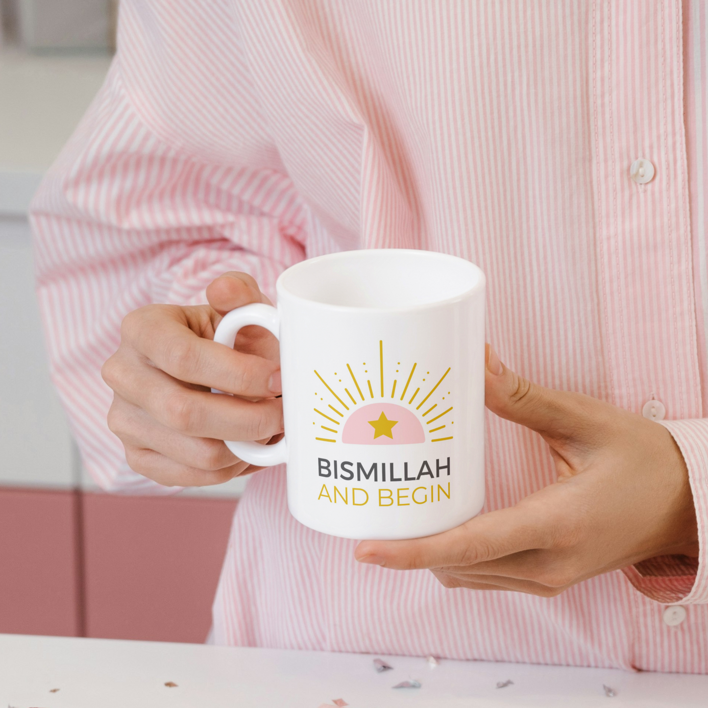 White mug with pink and gold sunrise design and text “Bismillah and Begin” in bold, modern typography.