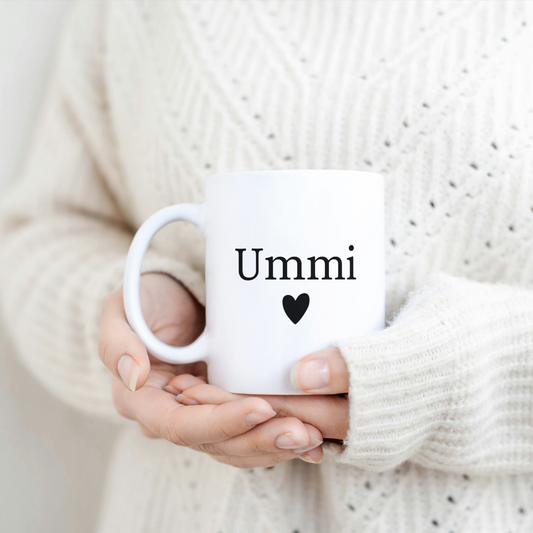 White mug with black “Ummi” and heart, held by woman in cozy cream sweater – elegant Islamic gift for mom.