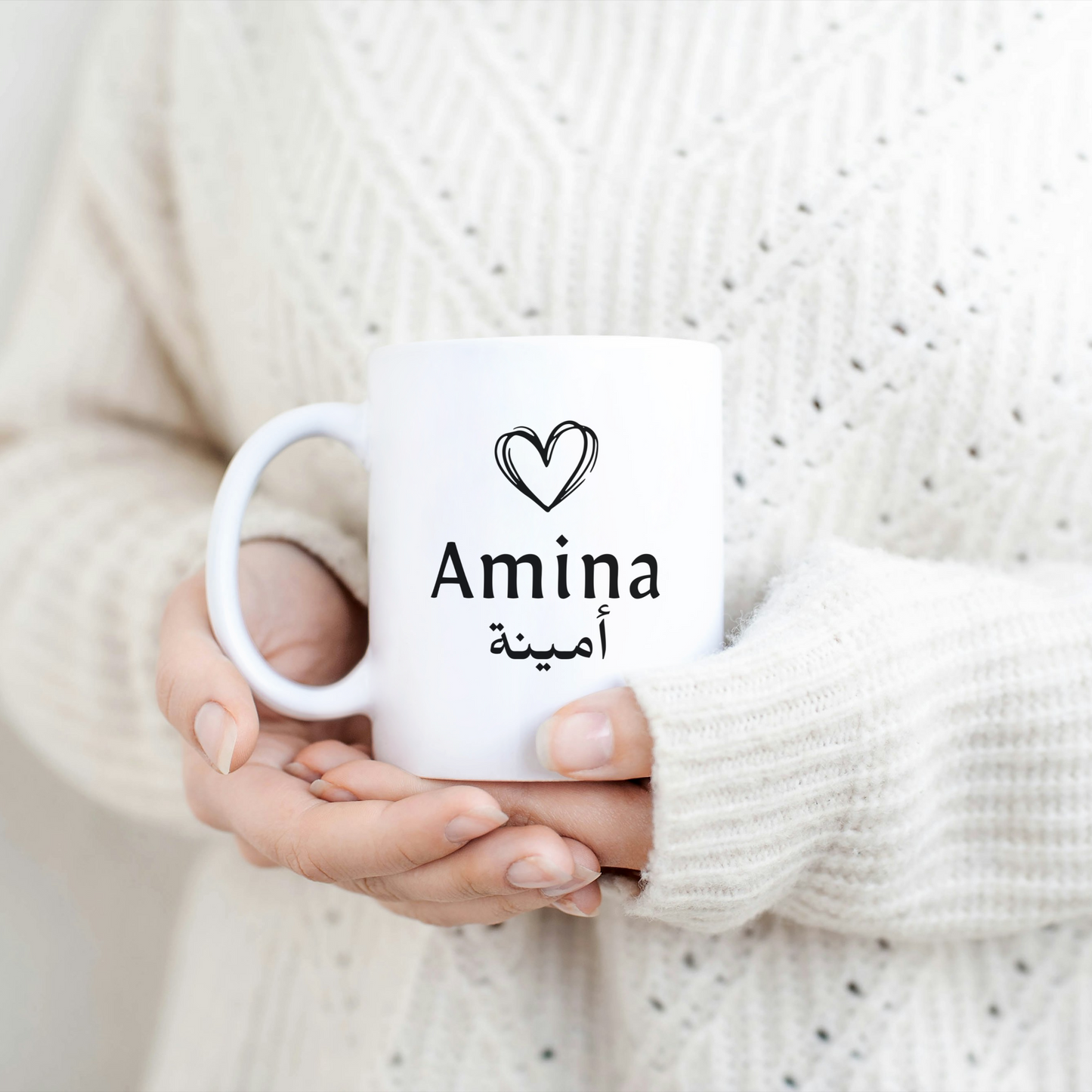 White mug with a black heart above a custom name in Arabic and English – styled on soft mint green blanket, minimalist Islamic gift.