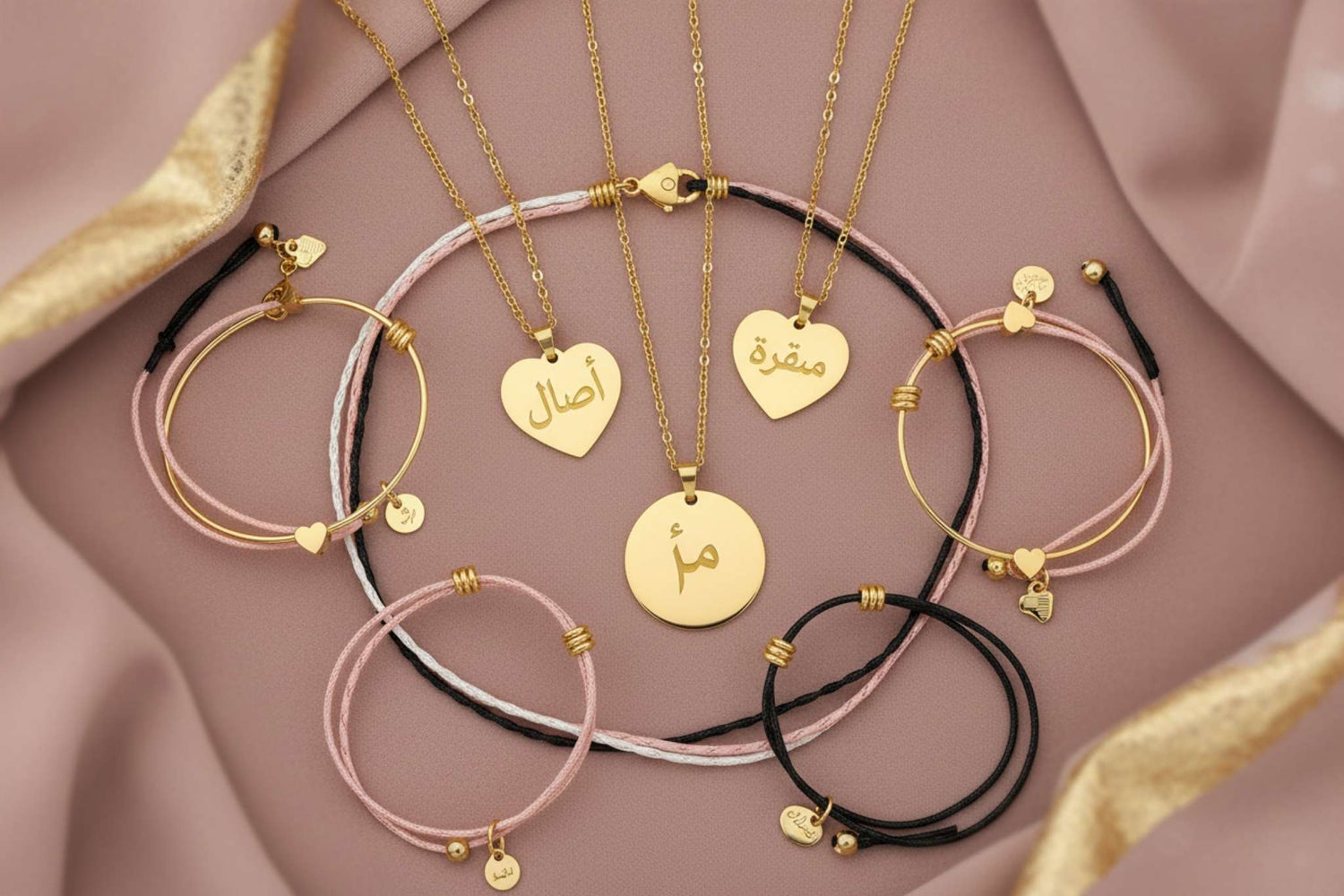 Jewelry collection flatlay - Custom Arabic name jewelry in gold on dusty pink background