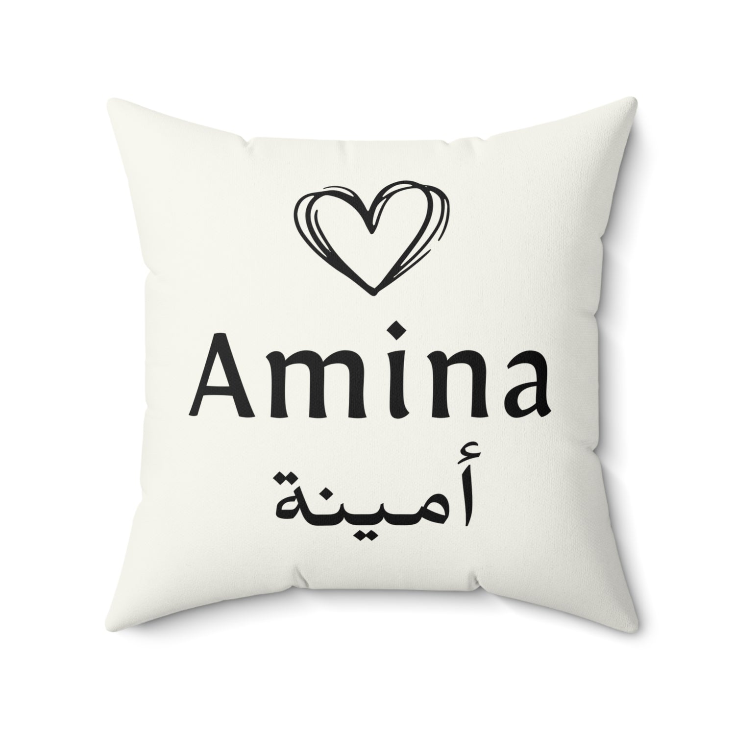 White pillow with the name “Amina” in English and Arabic (أمينة), topped with a black heart line drawing