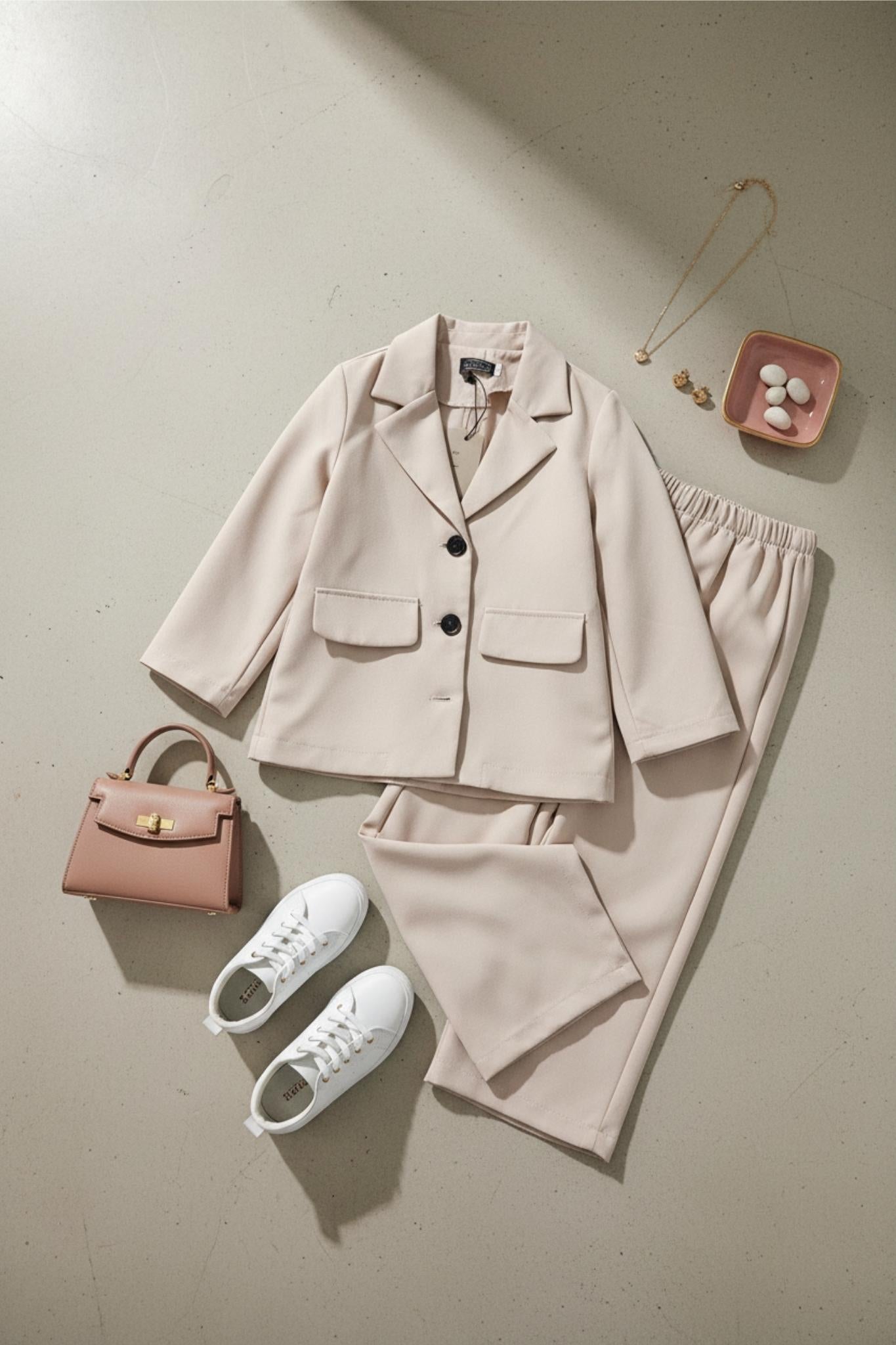 Beige outfit with jacket, pants, sneakers, and handbag on a light background