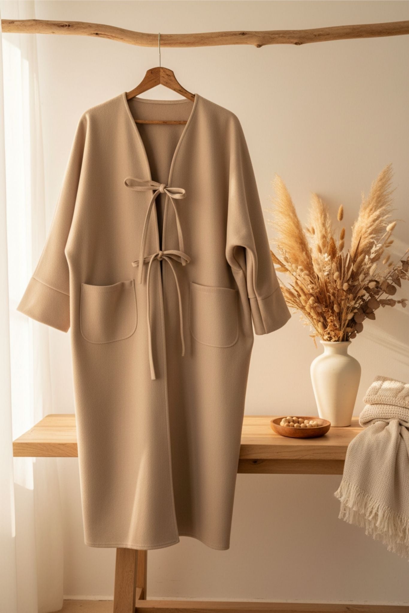 Beige coat hanging on a wooden hanger against a neutral background with decorative elements.