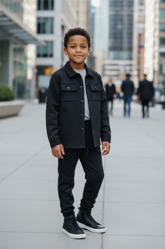 Child wearing a black jacket and pants standing on a city street.