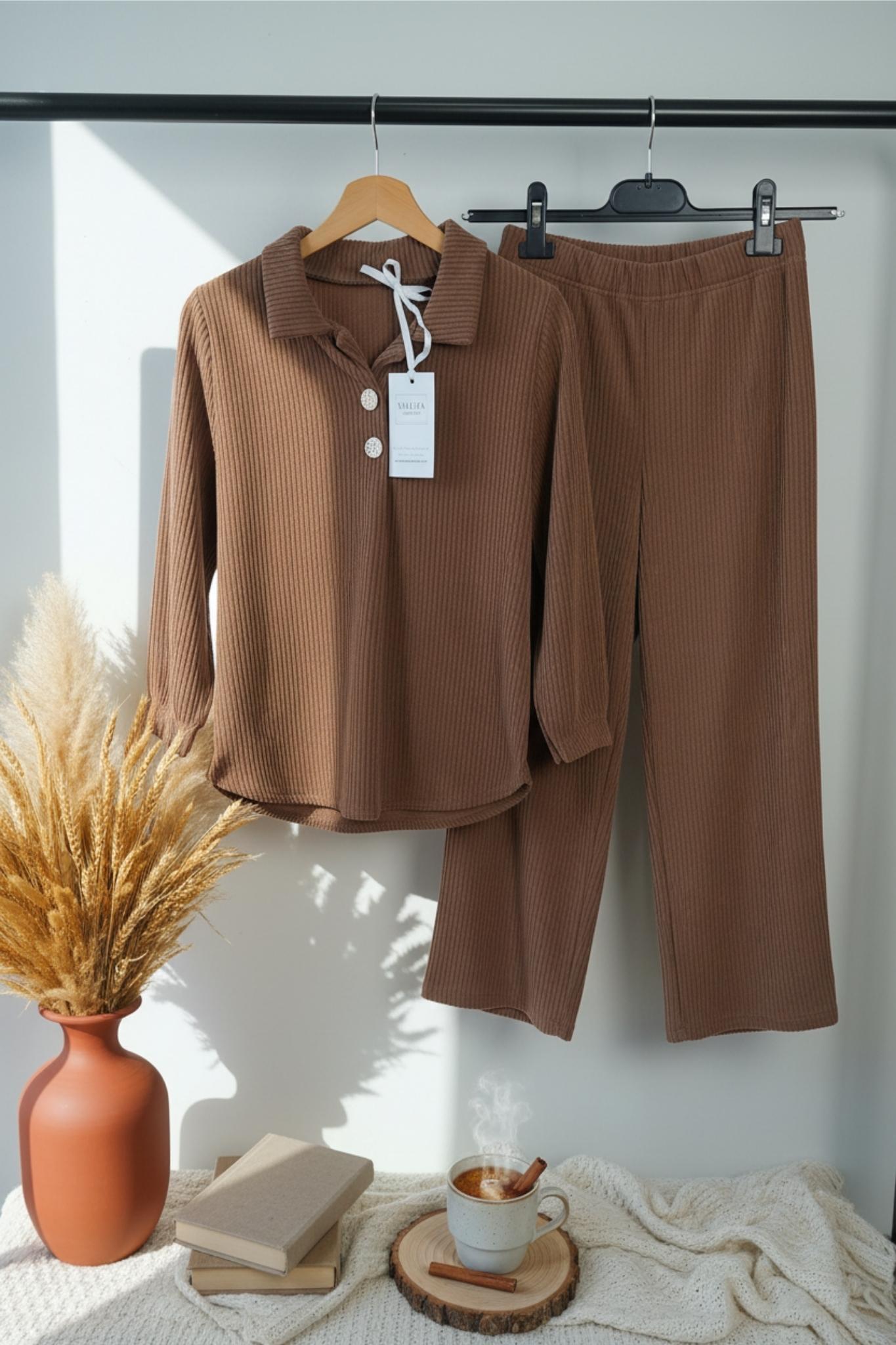 Brown suit on hangers with a vase, books, and cup on a table.