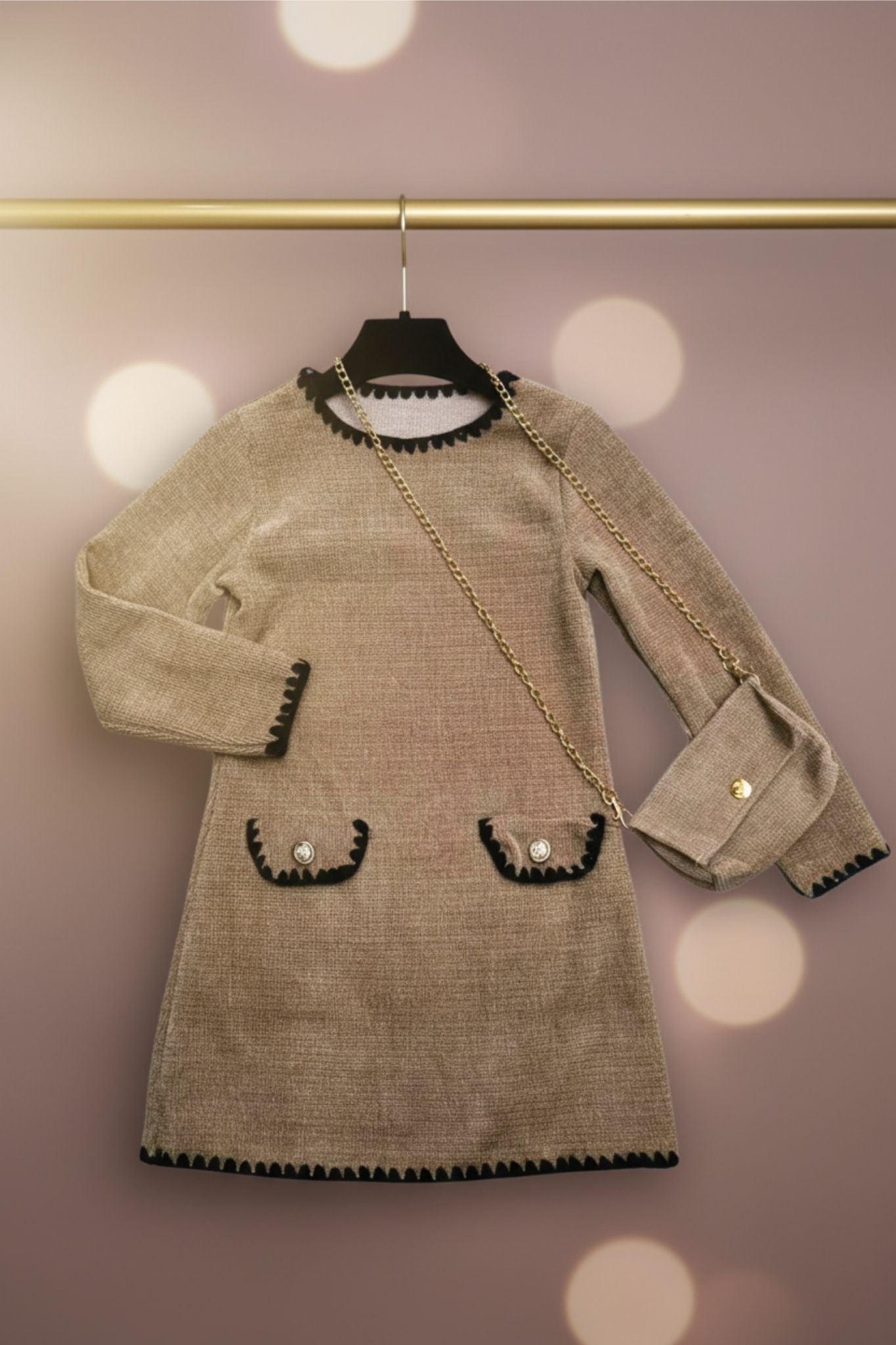 Taupe dress with black trim on a hanger against a blurred background